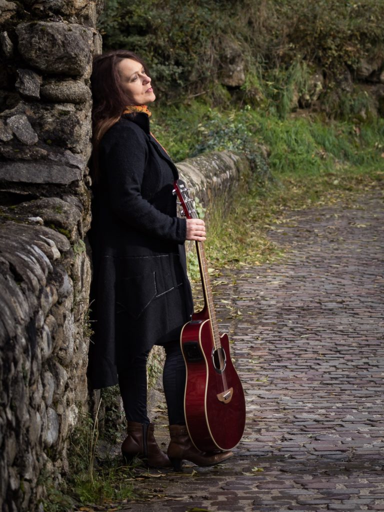 Muriel Batbie Castell avec sa guitare au bord d'un chemin - photo illustrant l'album "Par tous les chemins"